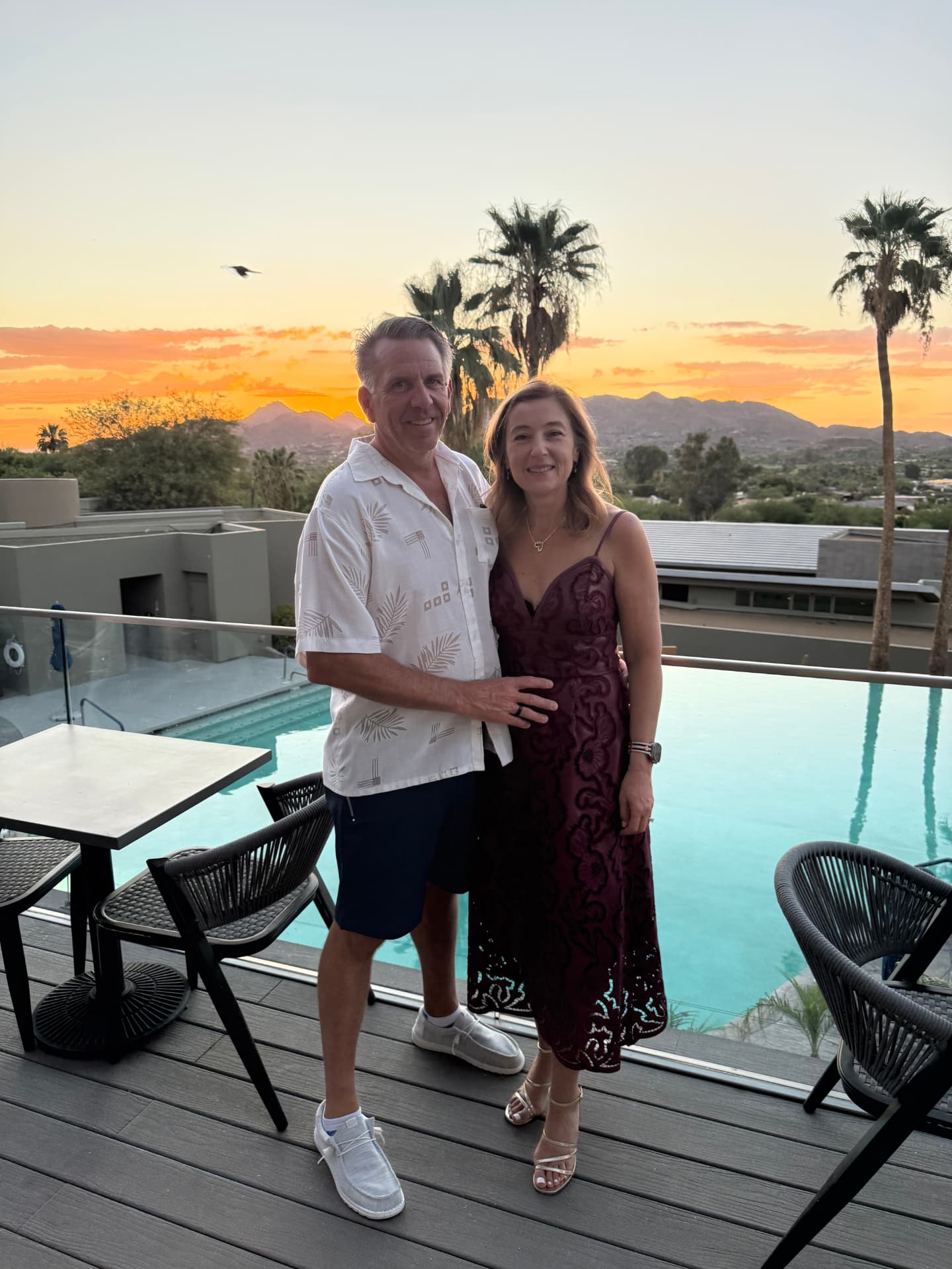 Natalia and her husband by a resort pool at sunset with palm trees and mountains