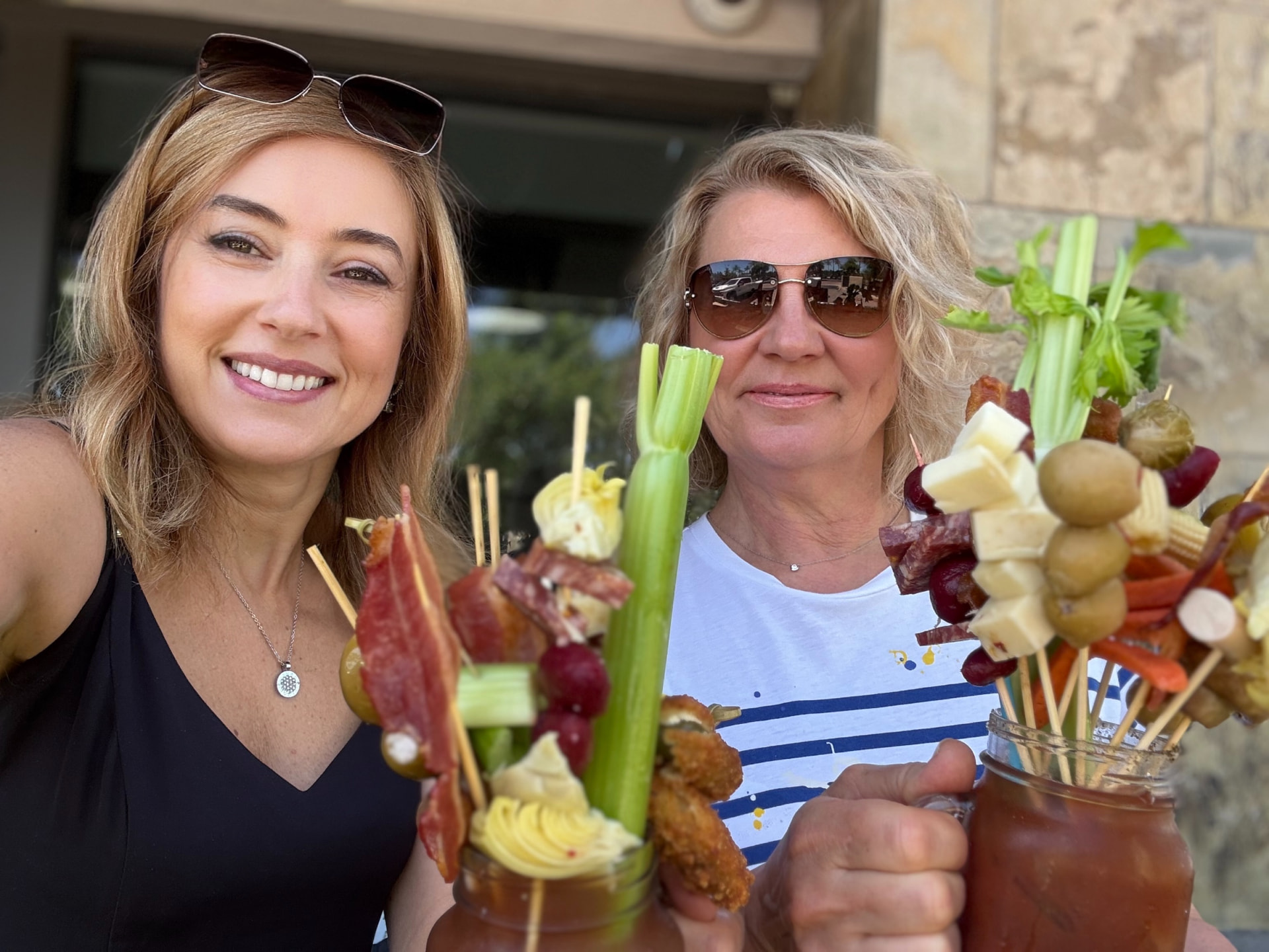 Natalia and a friend toasting loaded bloody marys at a sunny brunch