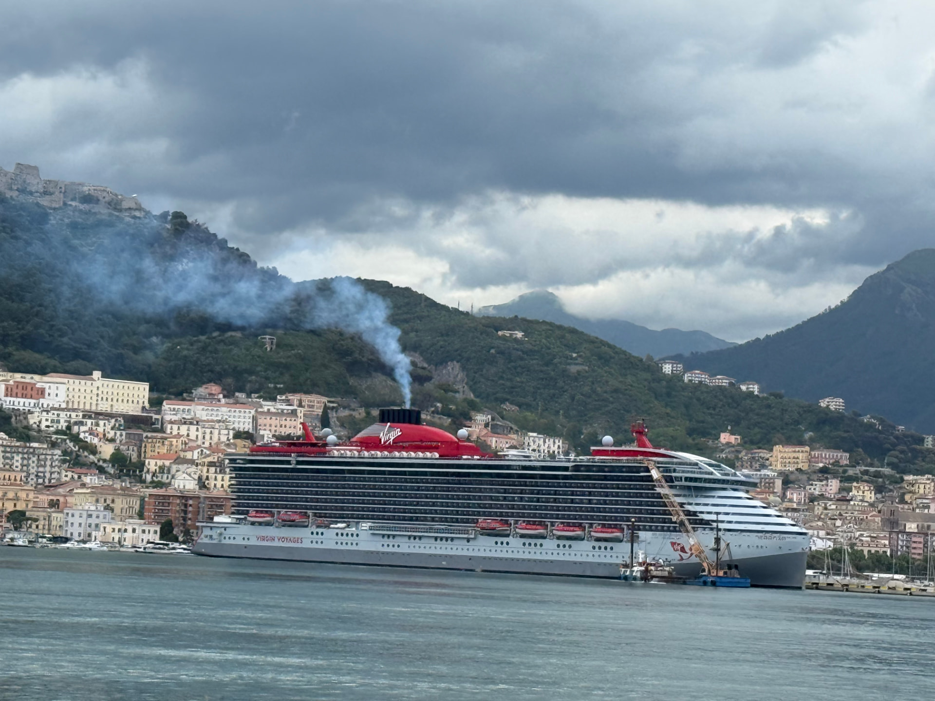 Virgin Voyages ship docked below the hills of an Italian coastal town