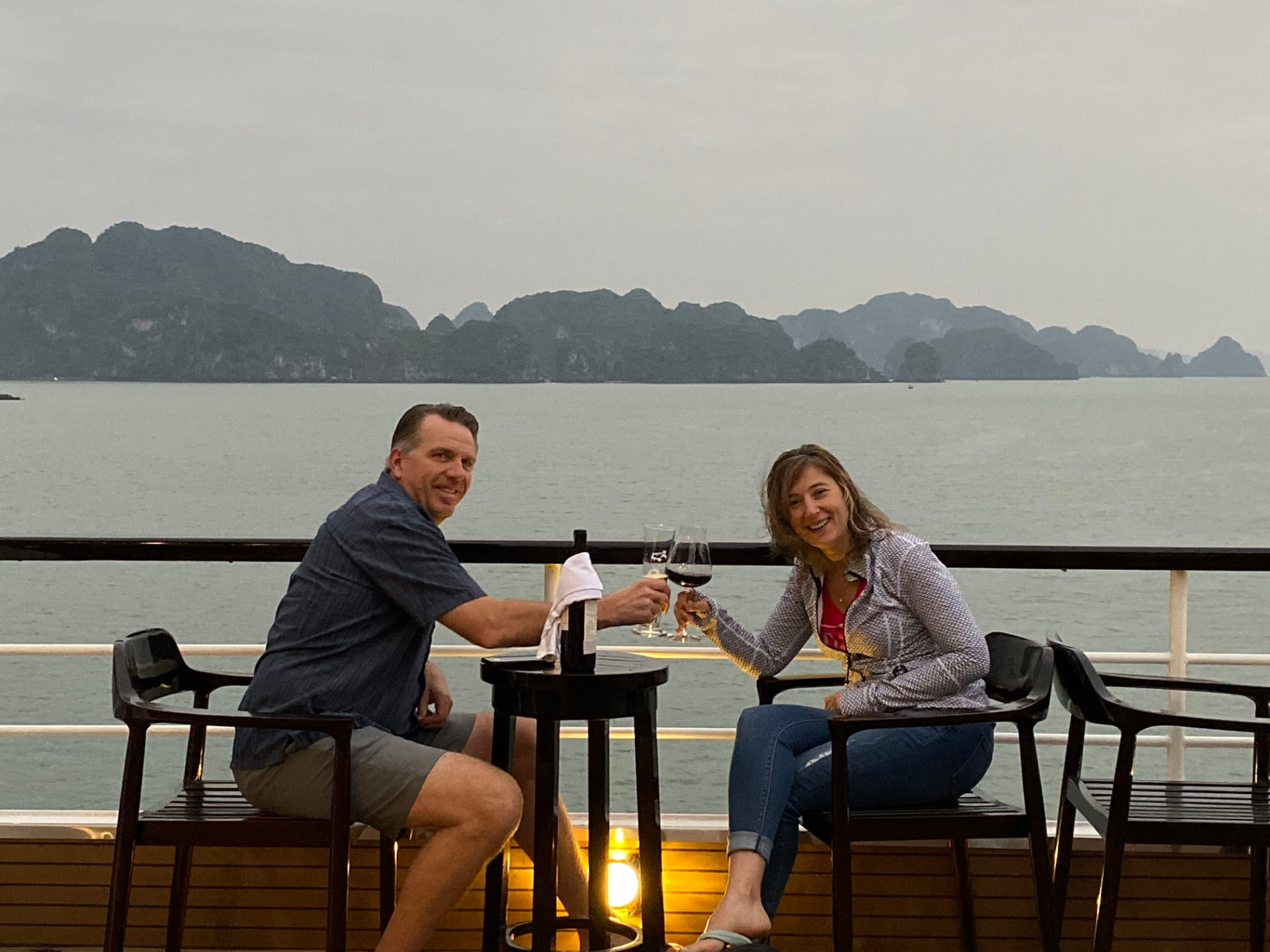 Couple toasting wine at a table on a cruise ship deck with limestone islands behind them
