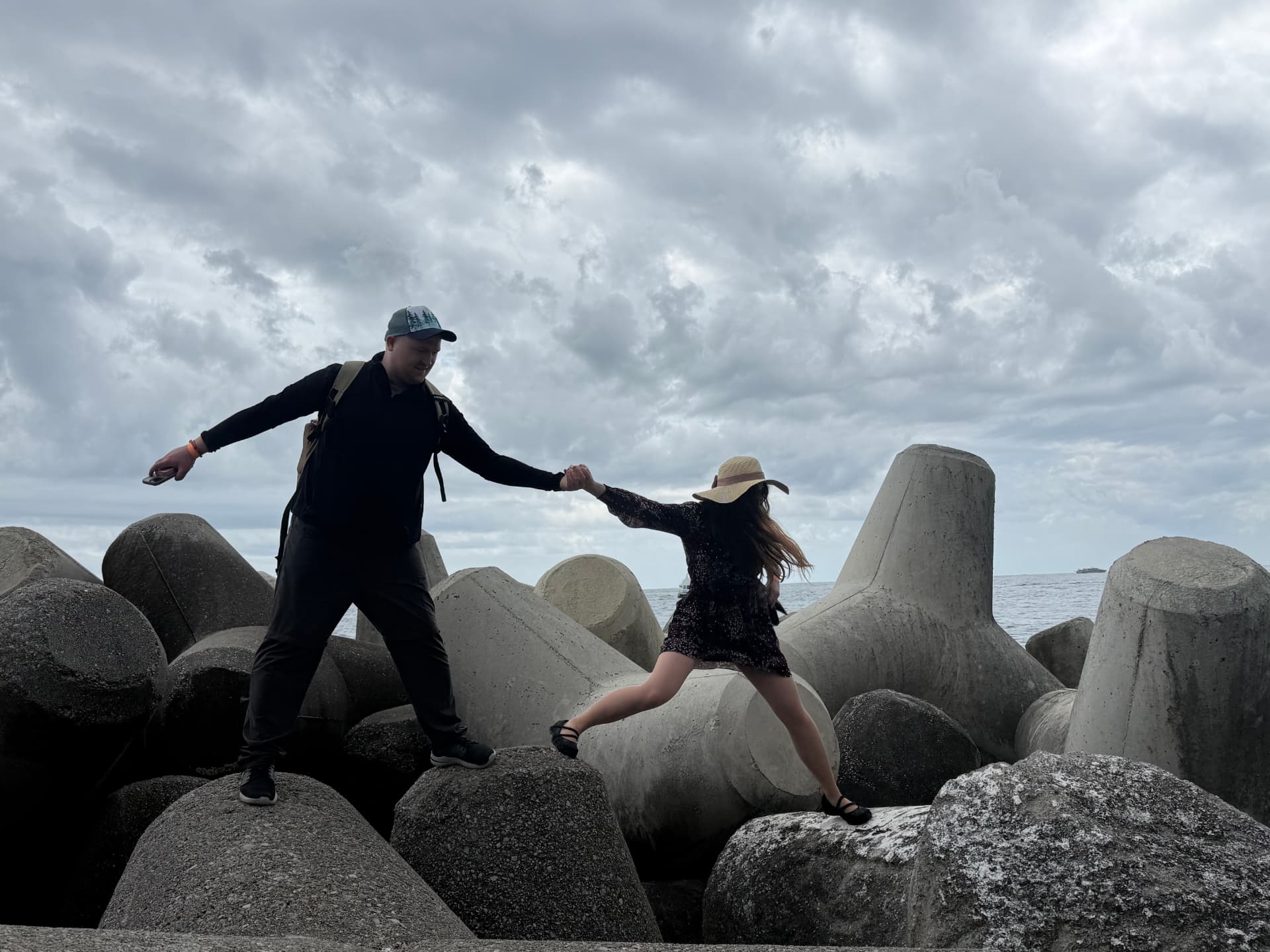 Couple stepping across concrete breakwater blocks by the sea